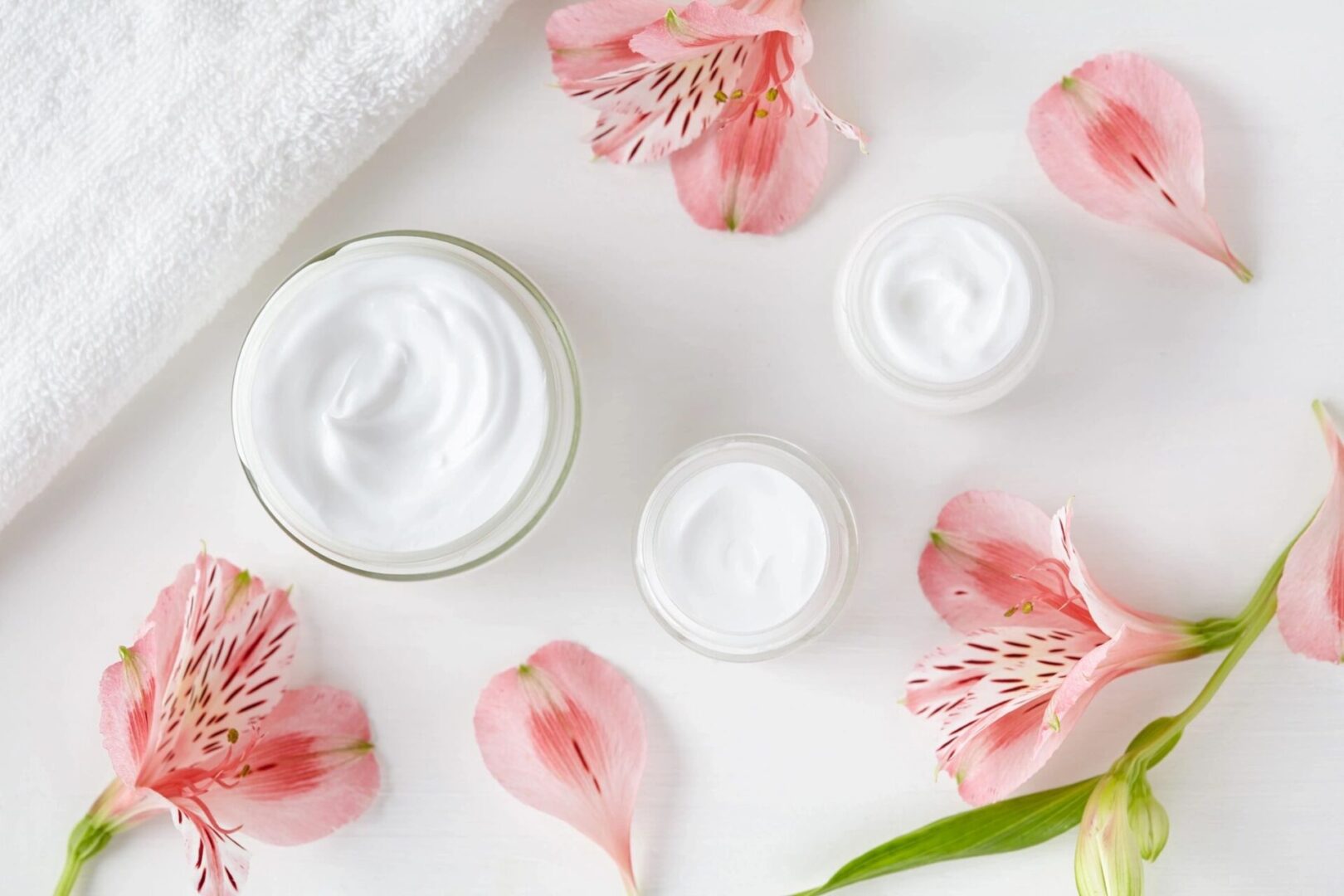 A white table topped with flowers and creams.