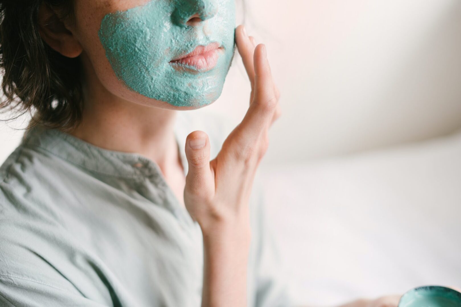 A woman with blue face mask putting cream on her face.