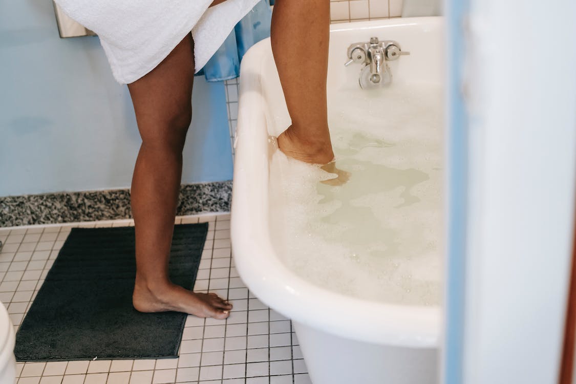 Woman stepping into bathtub full of bubbles.