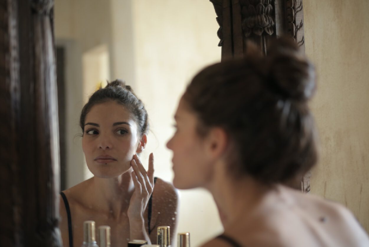 A woman looking at her reflection in the mirror.