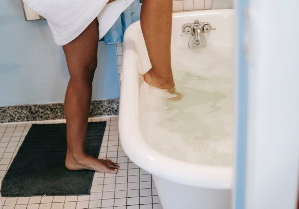 Woman stepping into bathtub full of bubbles.