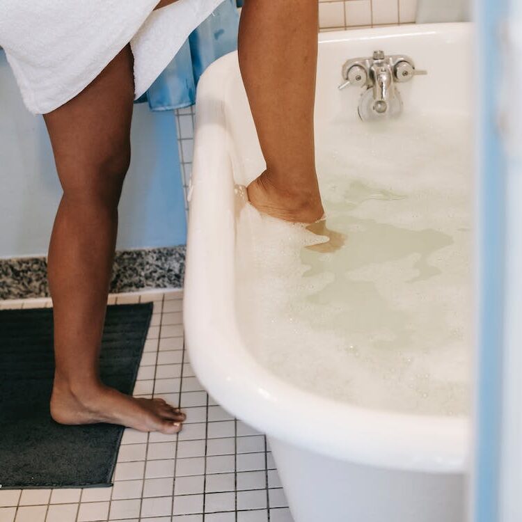 Woman stepping into bathtub full of bubbles.